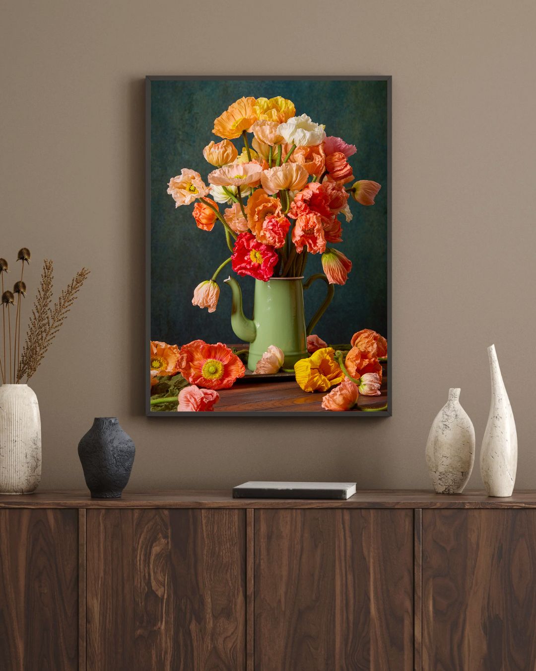 Poppy Passion, a framed painting of a green jug filled with bright flowers like pastel poppies, adorns the wall. Below, decorative vases stand on a wooden cabinet. The warm setting and neutral palette enhance the charm of this Italian canvas wall art.