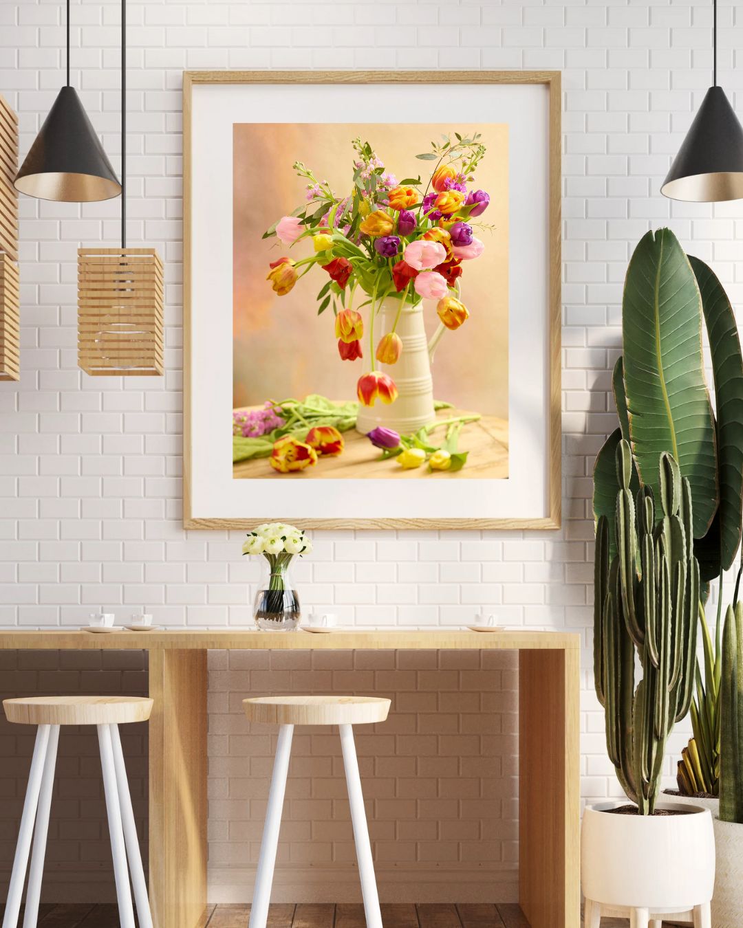 A modern dining area includes a high table with two white stools, with the Tulip Cascade print framed on a white brick wall, potted plants for greenery, and pendant lights creating a cozy atmosphere.