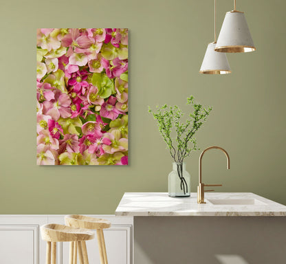 A kitchen with green walls showcases a large canvas of Hellebore Bed - Winter Roses. There is a marble countertop topped with a vase of green branches, a bronze faucet, and two wooden stools. Above, three cone-shaped pendant lights are suspended.