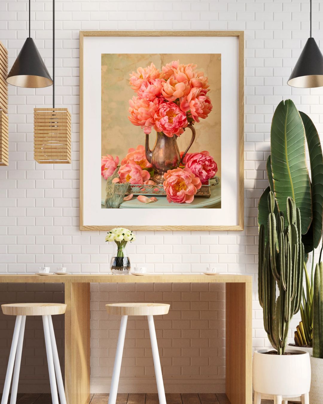 A modern kitchen with white brick walls displays Coral Radiance matted and framed. The space includes a wooden table, two white stools, pendant lights, and plants, creating an inviting atmosphere.