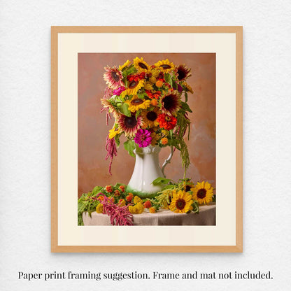 The Golden Fiesta as a framed fine art print featuring a vibrant bouquet of sunflowers, zinnias, and other flowers in a white vase on a table. The background exudes soft warmth. Frame and matting are suggested but not included.