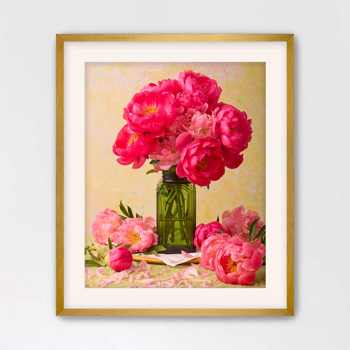 A framed image of a bouquet of pink peonies in a green vase, with additional pink peonies and a green vase on a table.