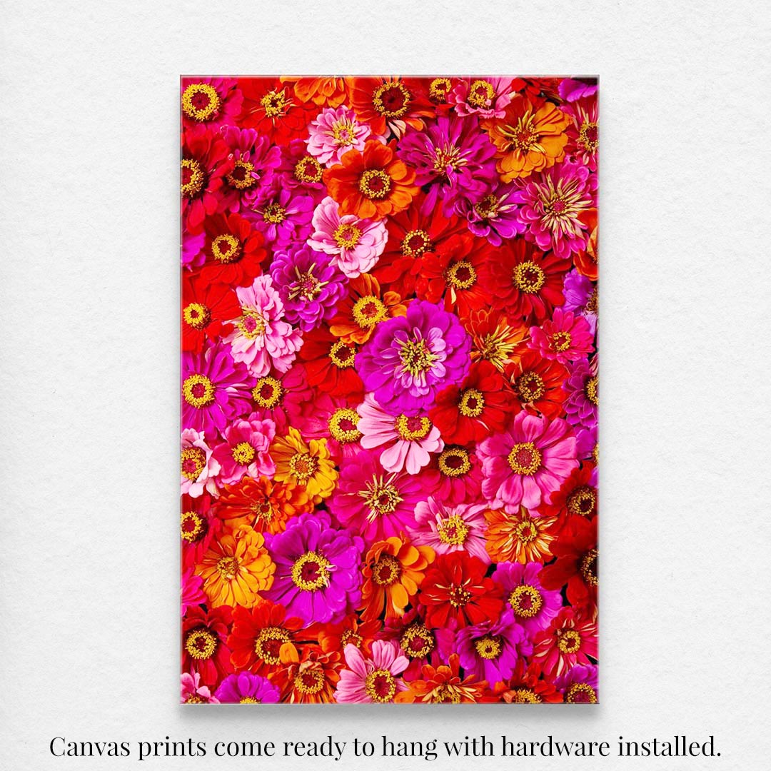 Zinnias Electric Radiance is a vibrant canvas wall art featuring densely packed pink, red, yellow, and orange zinnias on a bright background. This fine art paper print-style piece comes ready to hang with hardware installed.