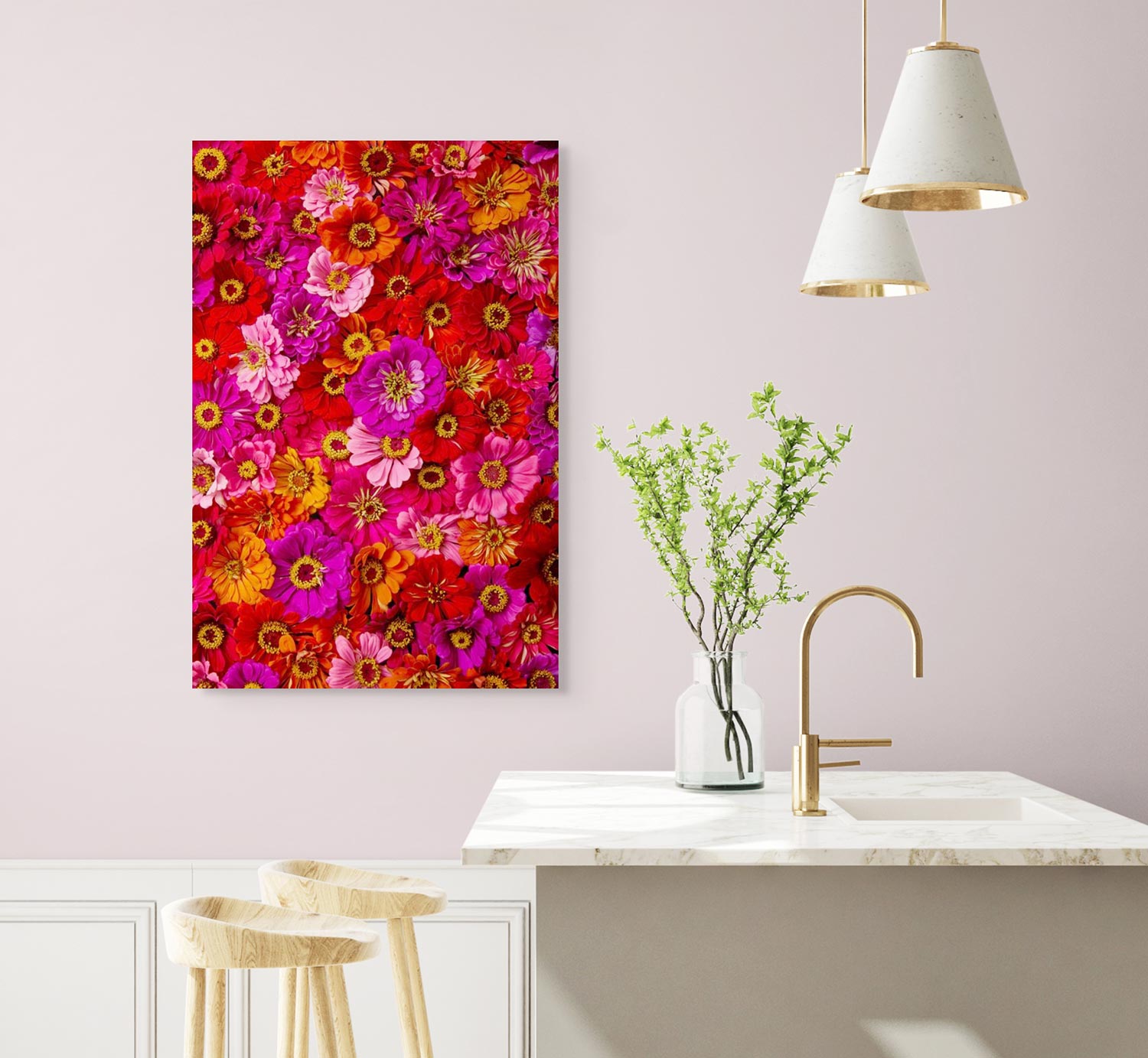 A bright, colorful canvas wall art titled Zinnias Electric Radiance hangs on a pale pink wall in a modern kitchen. The space features a marble countertop, two wooden stools, and a small plant in a vase with two pendant lights illuminating the counter.