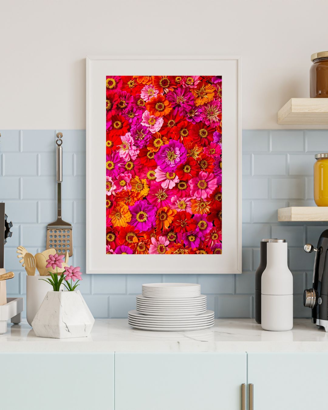 A kitchen counter with stacked white plates, utensils in a holder, and a potted plant. The tiled backsplash displays Zinnias Electric Radiance, a colorful canvas wall art featuring vibrant red, pink, and orange zinnias.