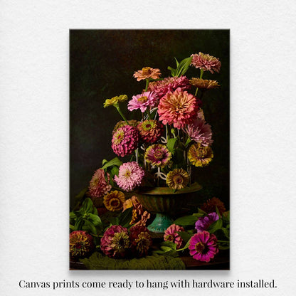 The Petals In Flight wall art as a canvas print of vibrant pink, orange, and purple zinnias set against a dark background. Featuring zinnias in a birdcage for added interest, this piece comes ready to hang with hardware installed.