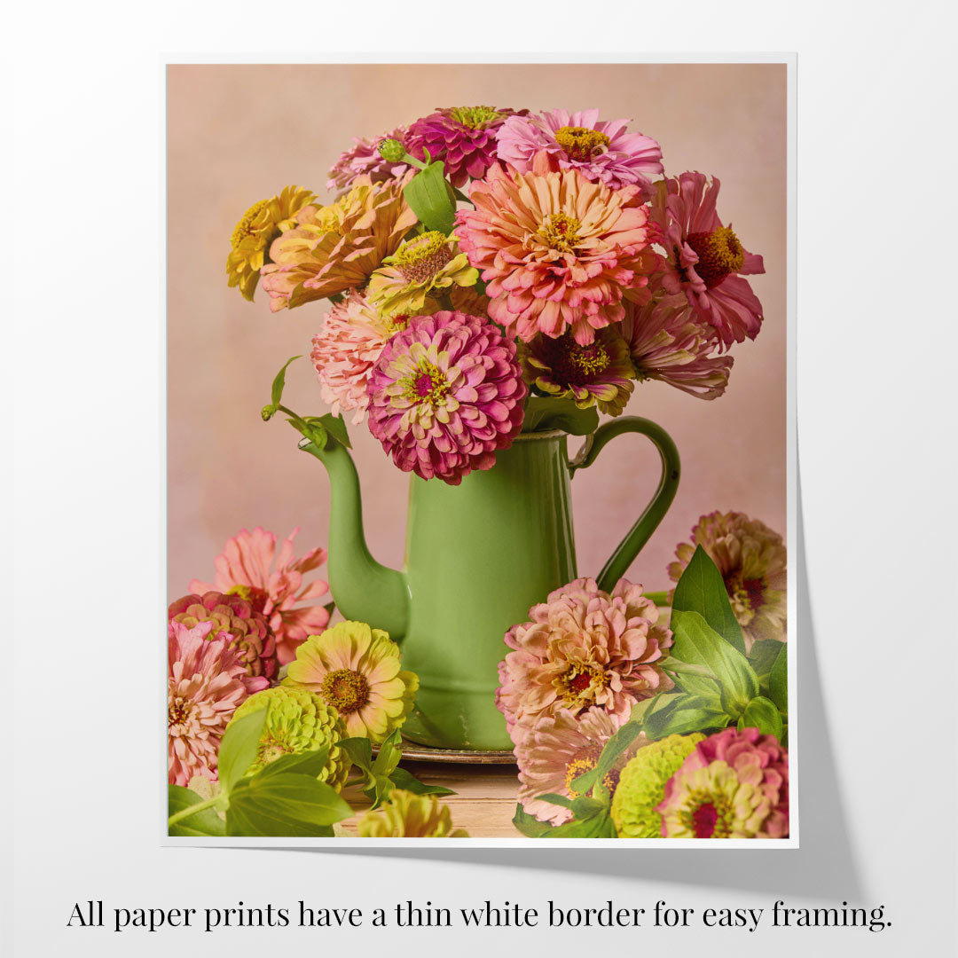 The Steeping Beauty features a colorful bouquet, mainly pink and yellow, artistically arranged in a vintage green teapot. With a soft beige background, this fine art paper print includes a thin white border for easy framing.