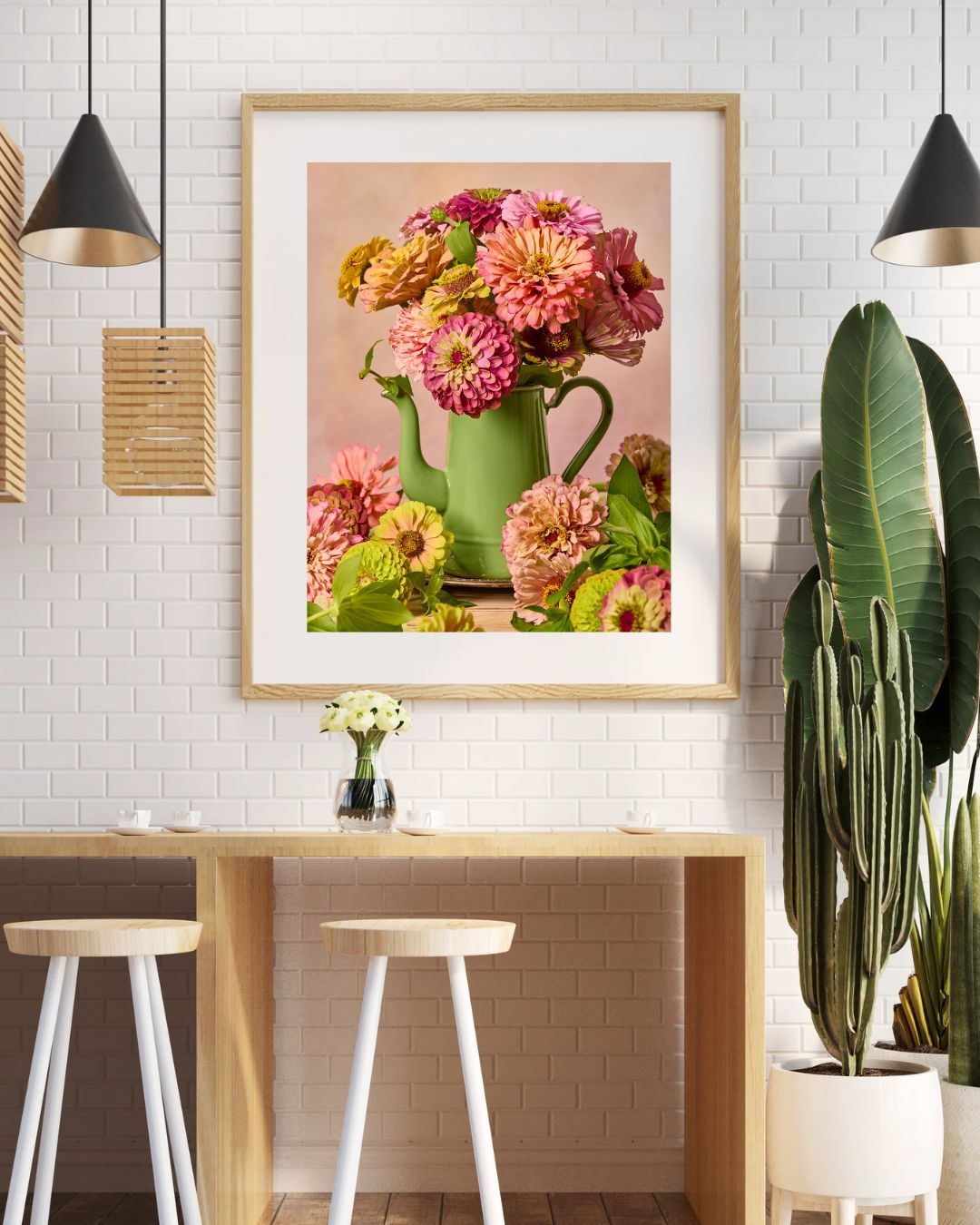 The Steeping Beauty dining area includes two stools and a wooden table, with framed floral canvas wall art above. The room features white brick walls, hanging lamps, and vibrant green plants, including a right-side cactus.