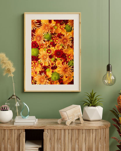 A sage green wall displays Chrysanthemum Bed - Autumns Embrace art print in a white mat and light wood frame. Below, a wooden console is adorned with books, decor, plants, and a hanging bulb, enhancing the cozy autumnal palette of this stylish interior.