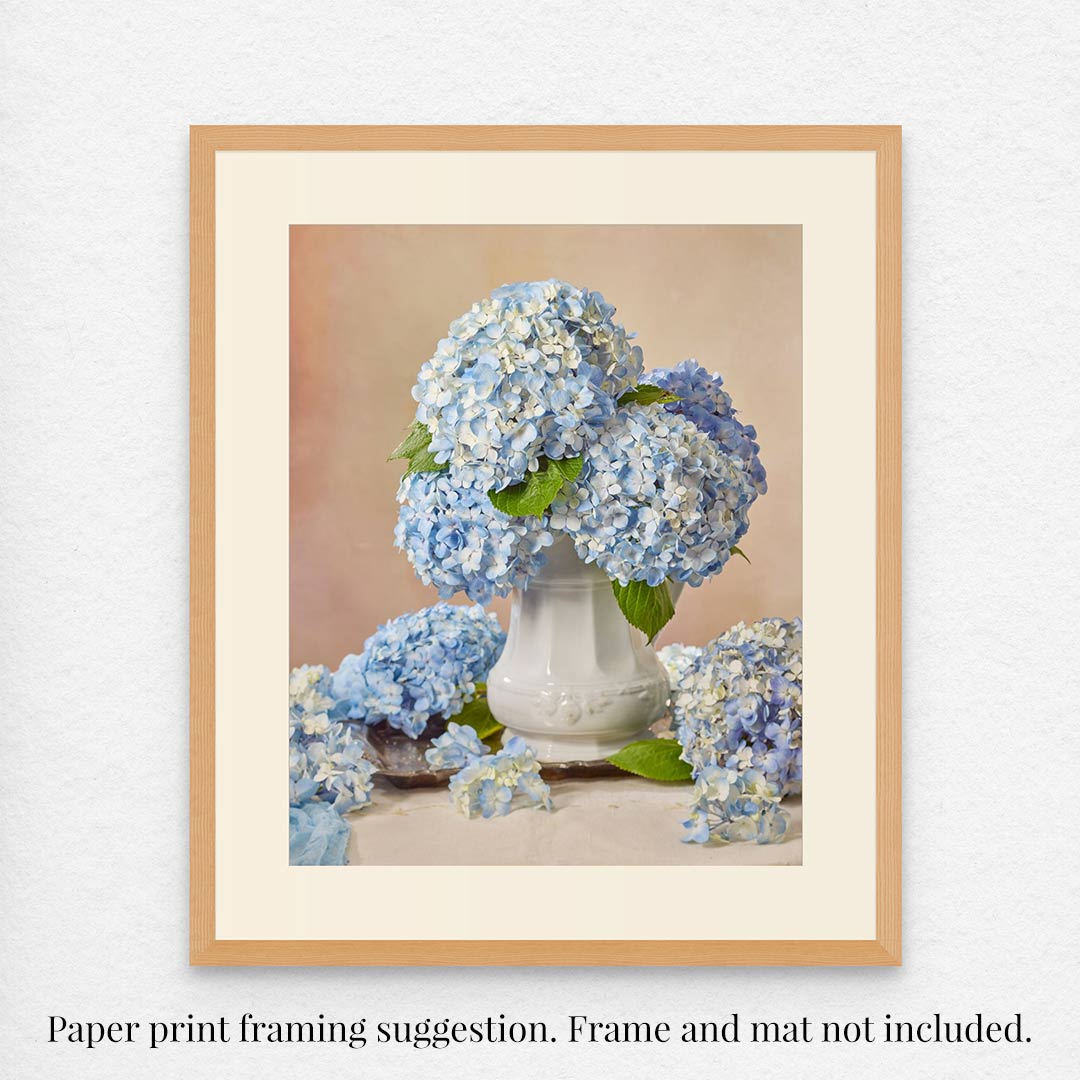 A photo titled Dreaming of Something Blue features blue hydrangeas in a white vase, surrounded by flowers, displayed in a wooden frame with a cream mat. Below it reads: Fine art paper print framing suggestion. Frame and mat not included.