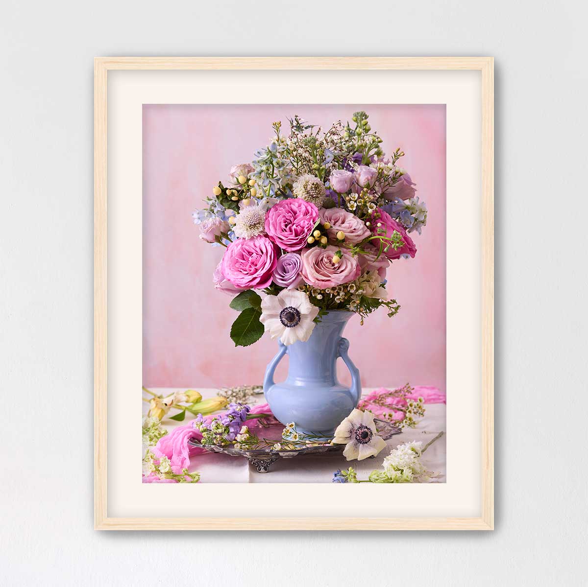 A framed image of a vase filled with a variety of colorful flowers, including pink roses, white lilies, and purple and white flowers, set against a pink background.