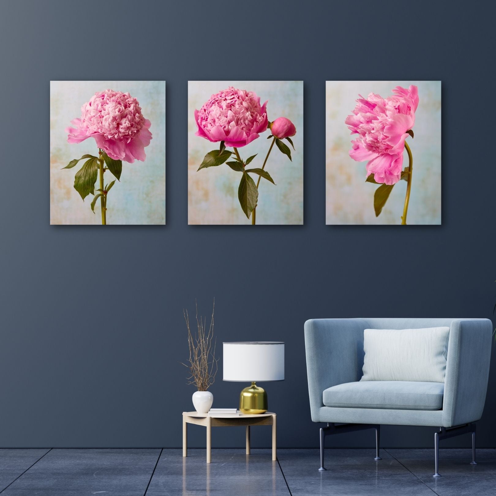 The Peony Sister Portraits - 3 Piece set is showcased on a dark wall above a modern light blue couch with a cushion. A small table beside the couch holds a decorative vase and gold-colored object, infusing the space with timeless romance.