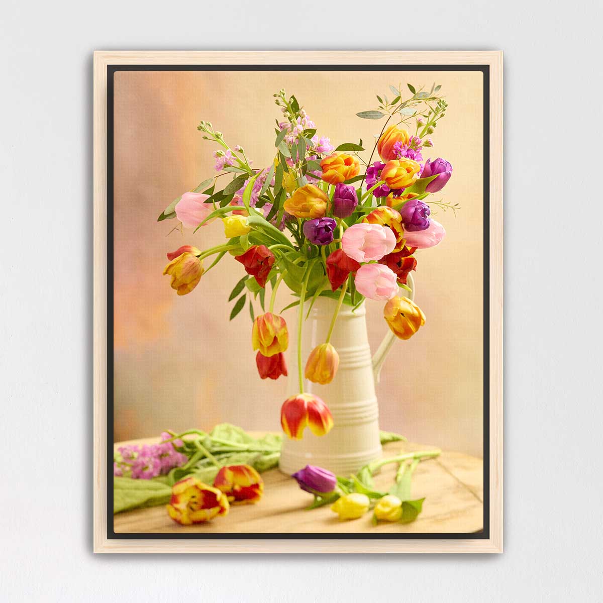 A white vase filled with a vibrant bouquet of tulips in various colors, including pink, yellow, and purple, sits on a wooden surface.