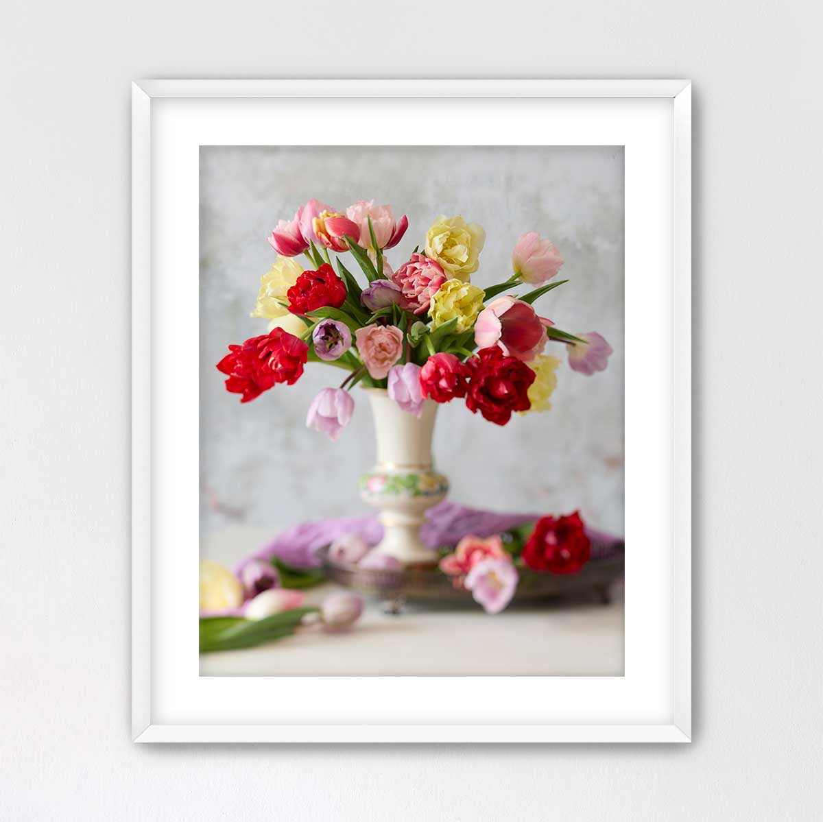 A white vase filled with a vibrant bouquet of red, pink, yellow, and white flowers sits on a table, creating a visually appealing and colorful still life.