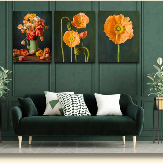 In a dark green living room, a velvet sofa with black and white patterned cushions is complemented by the Poppy Sisters Portraits - 3 Piece art set of orange flowers above it. Two potted plants flank the sofa.