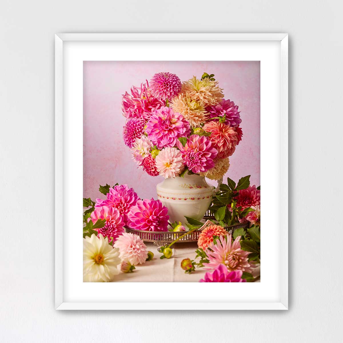 A white vase filled with a vibrant bouquet of pink and yellow dahlias sits on a table, surrounded by additional flowers.