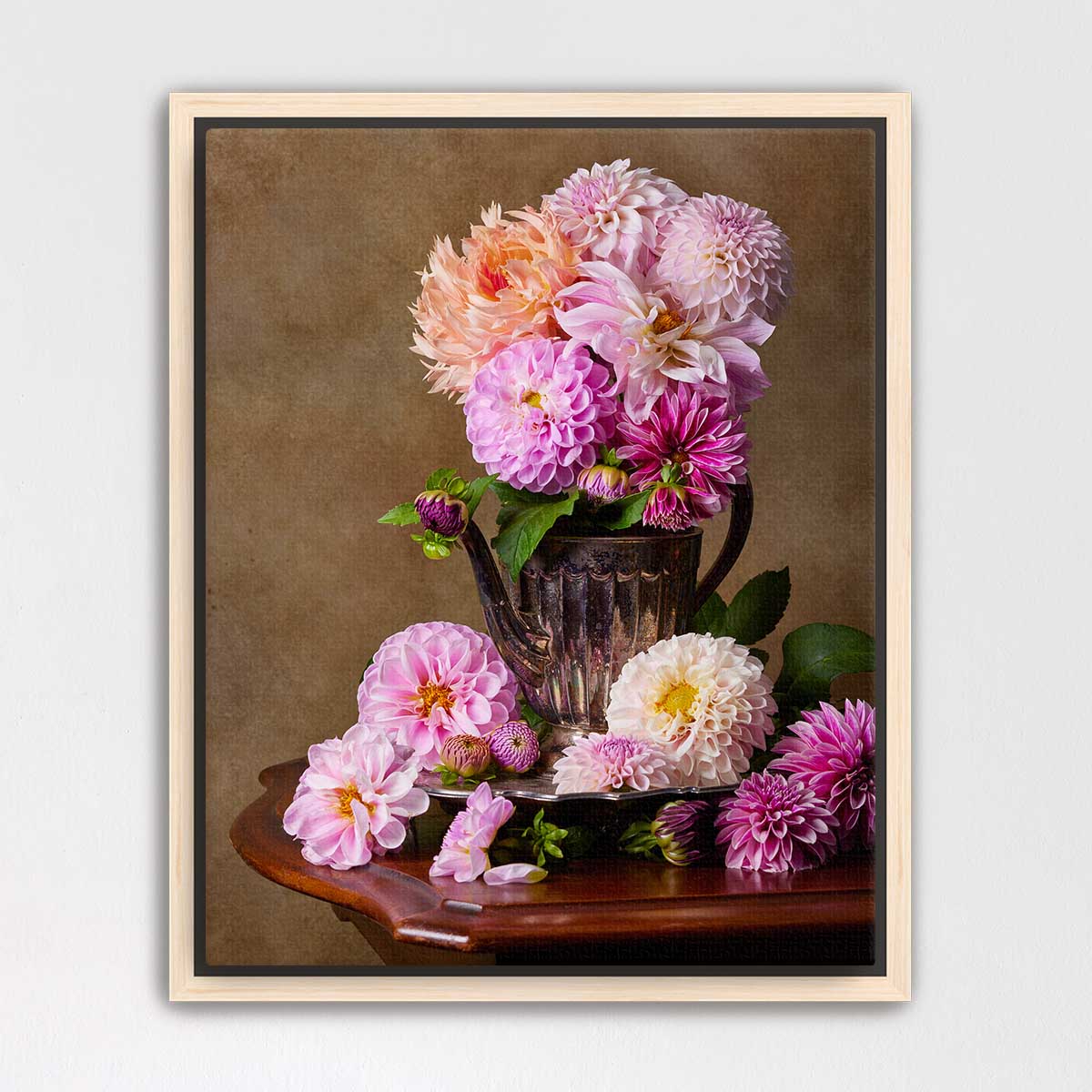 A vase filled with a variety of colorful dahlias sits on a wooden table, surrounded by additional dahlias.