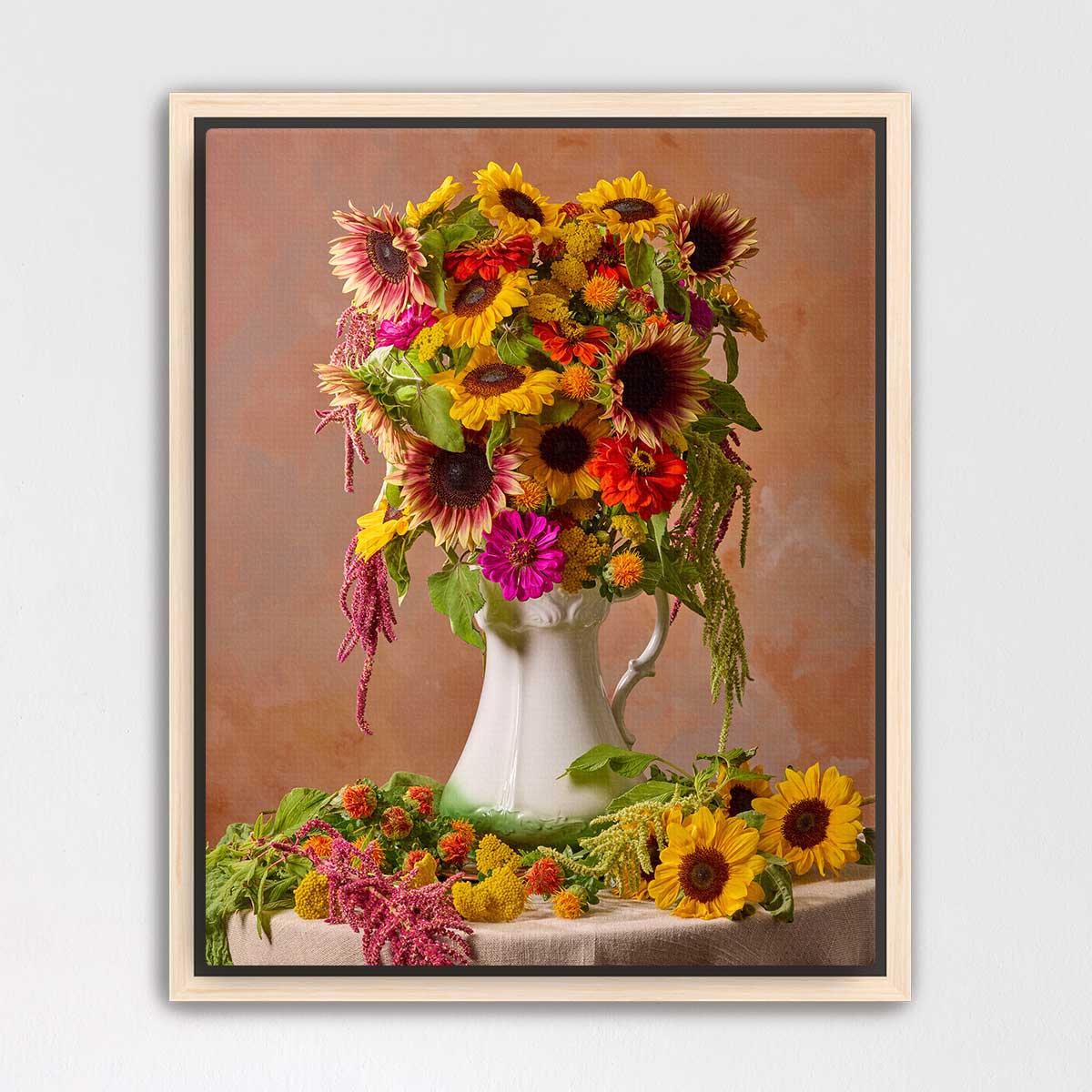 A white vase filled with a vibrant bouquet of sunflowers and other colorful flowers sits on a table, surrounded by additional flowers.