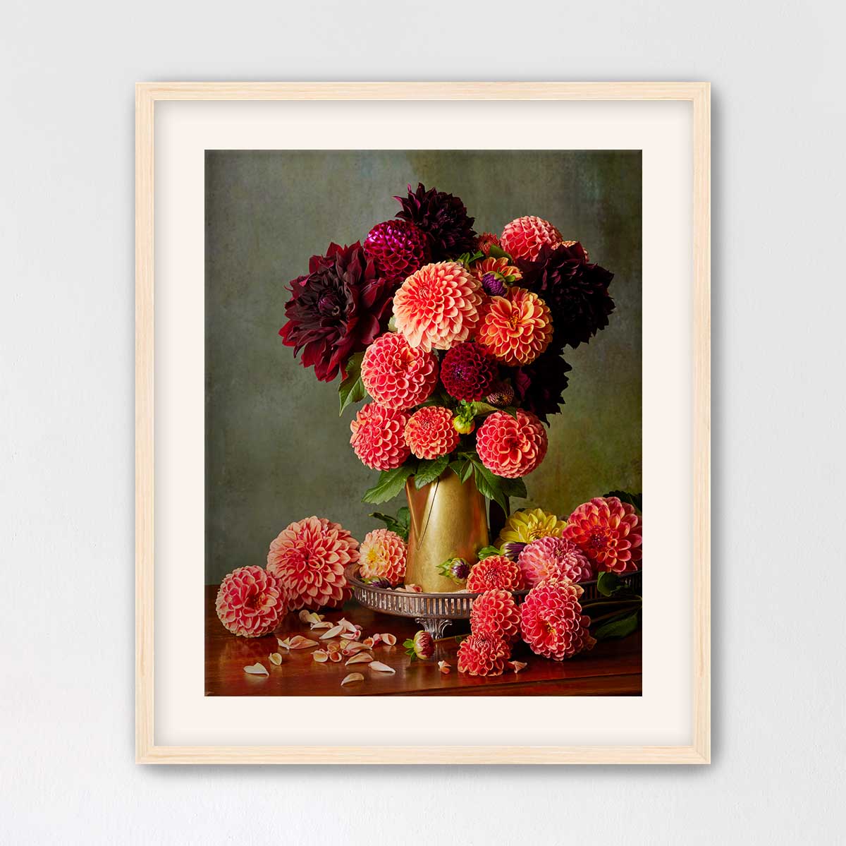 A framed still life painting depicting a vase filled with a variety of colorful dahlias, including red, pink, and yellow flowers, placed on a wooden surface.