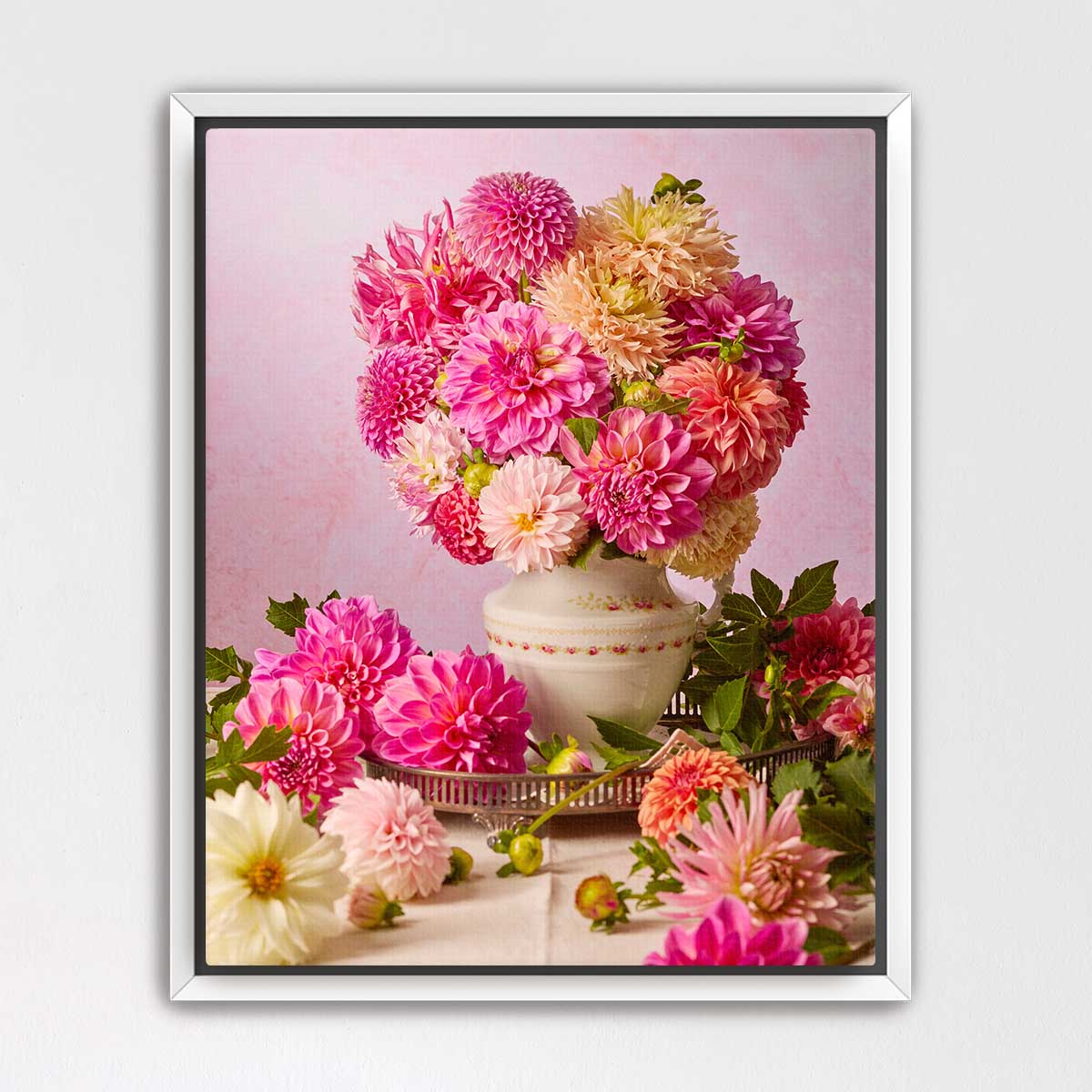 A white vase filled with a vibrant bouquet of pink, yellow, and orange dahlias sits on a table, surrounded by additional flowers.