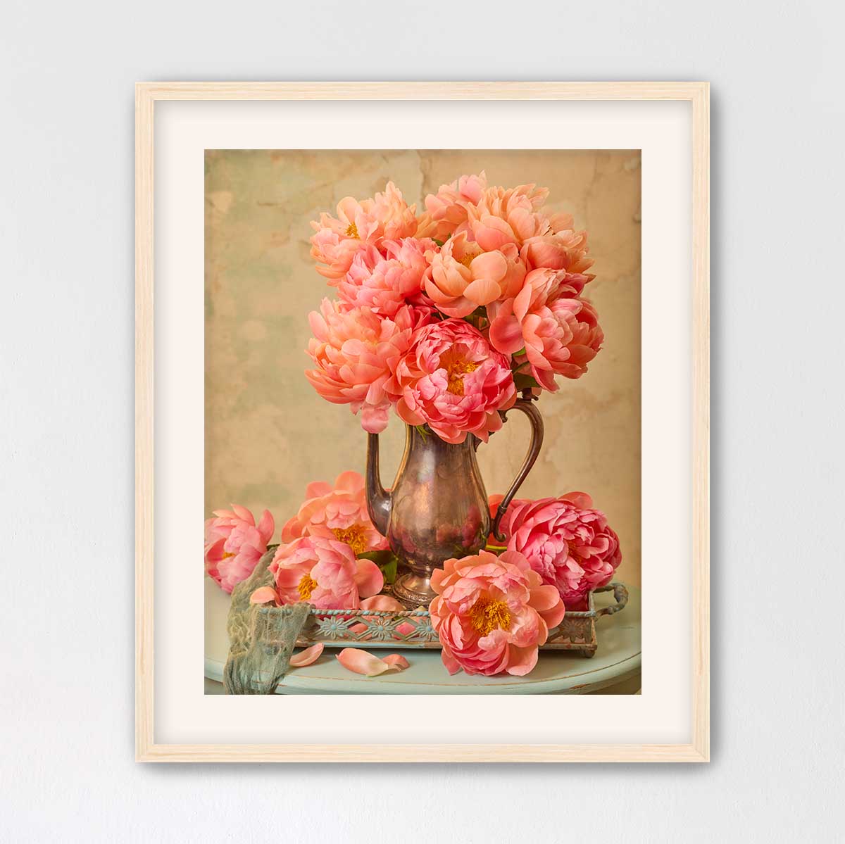 A framed image of a vase filled with vibrant pink peonies, placed on a small table.