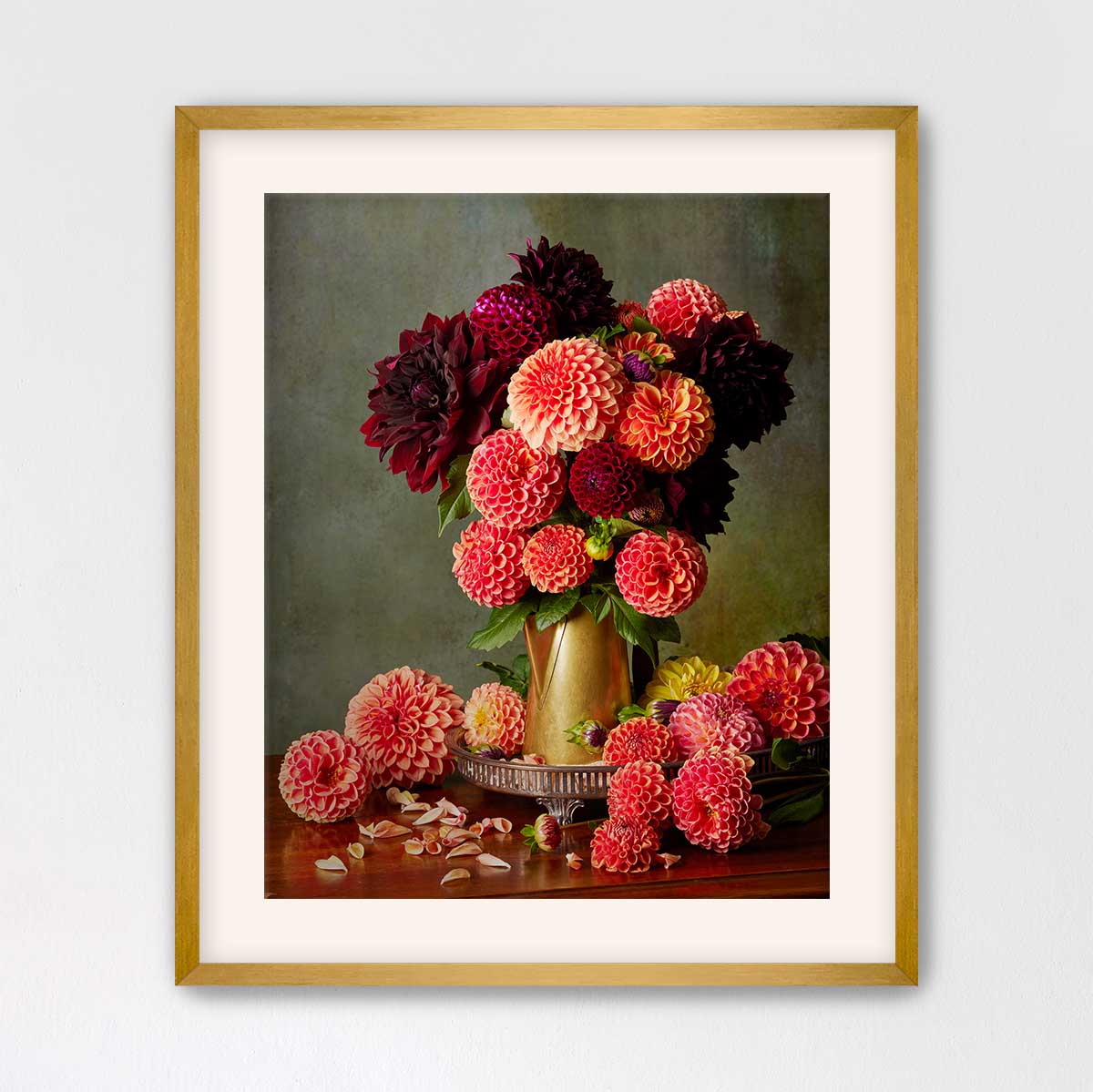 A framed still life painting depicting a vase filled with a variety of colorful dahlias, including red, pink, and yellow flowers, placed on a wooden surface.