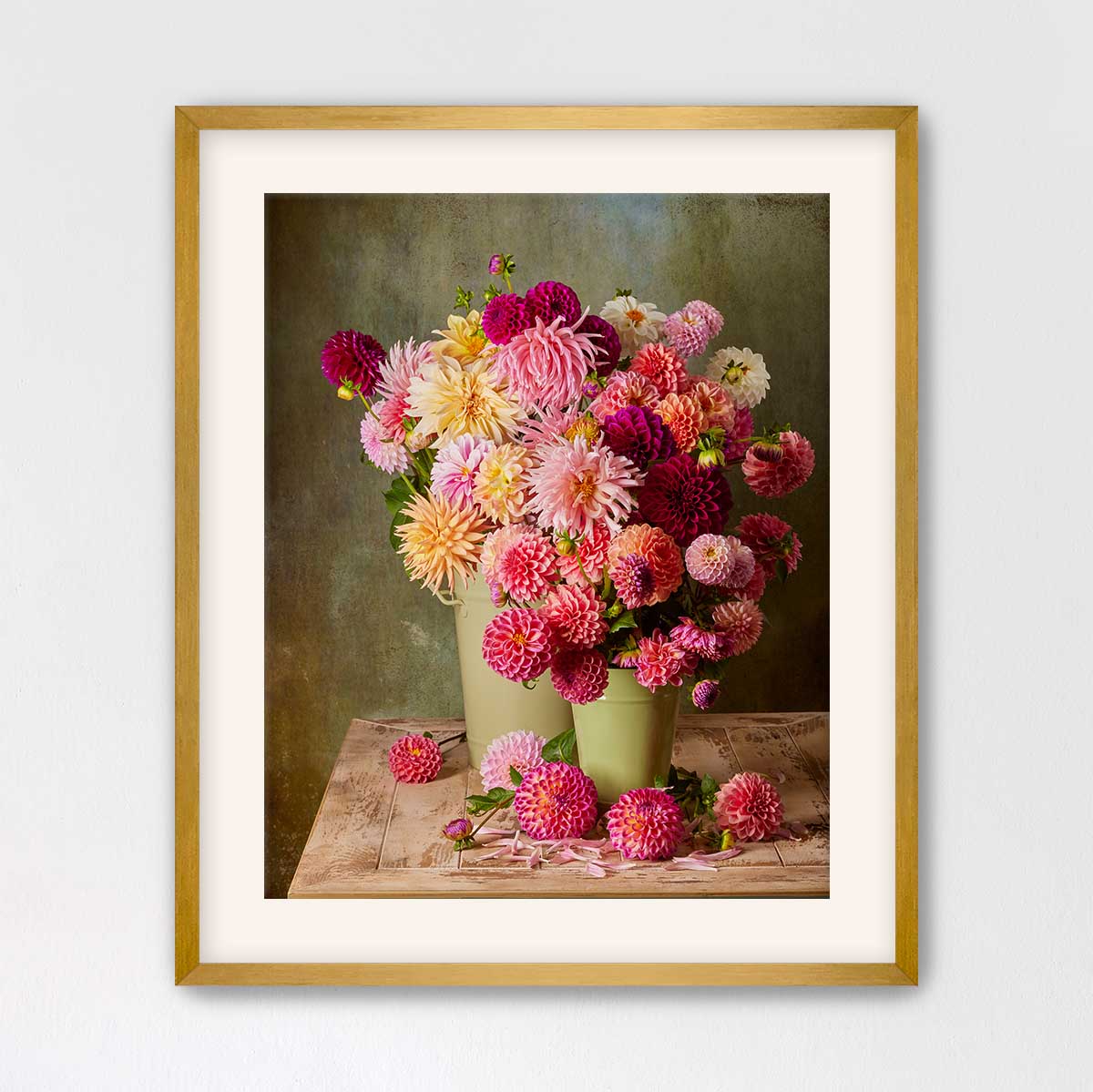 A framed image of a bouquet of colorful dahlias in a vase, with some flowers spilling out of the vase and scattered on the table below.