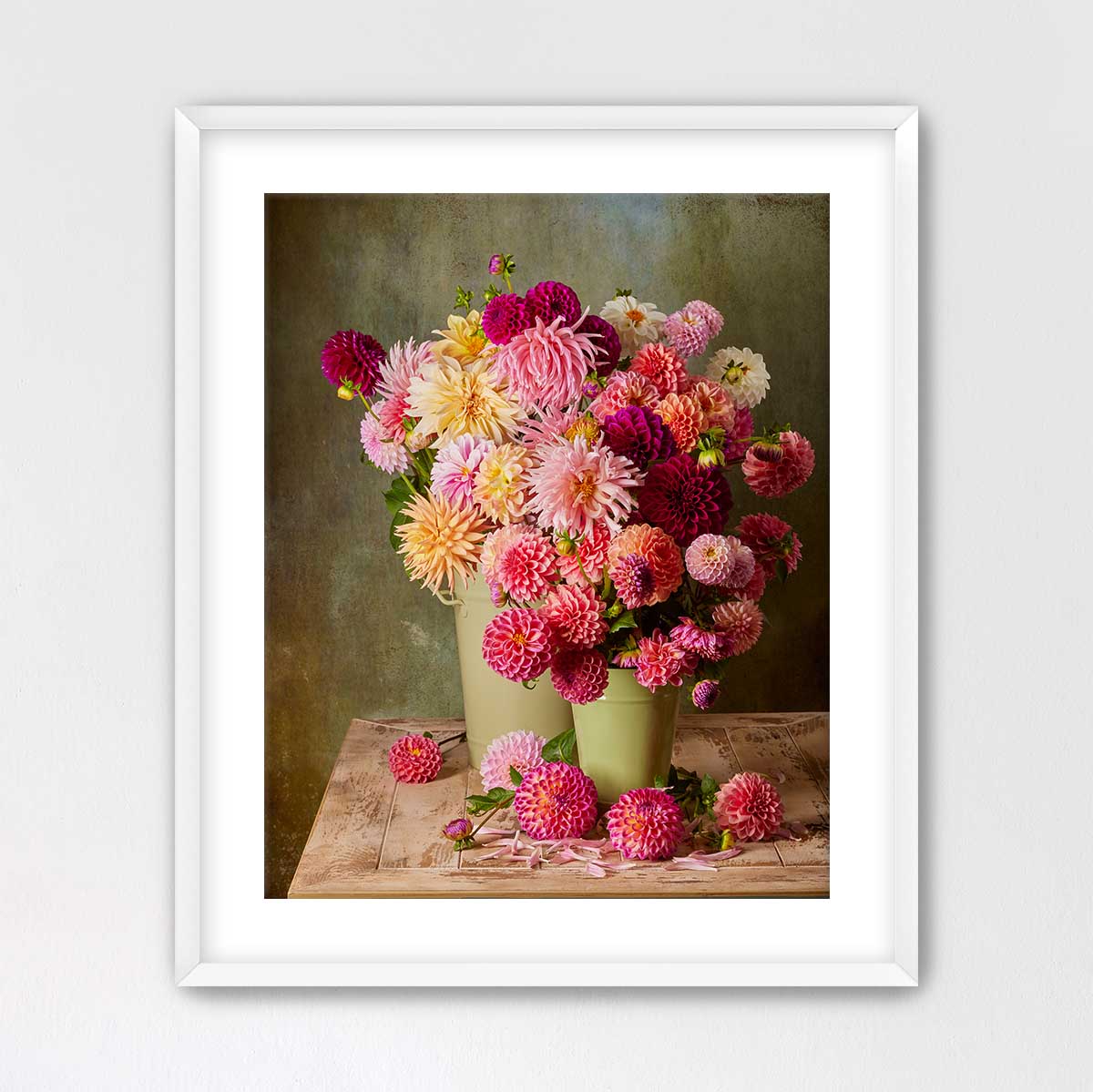 A framed image of a bouquet of colorful dahlias in two green vases, placed on a wooden surface.