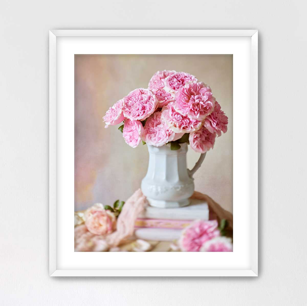 A white vase filled with pink carnations sits on top of a stack of books, creating a charming and elegant scene.