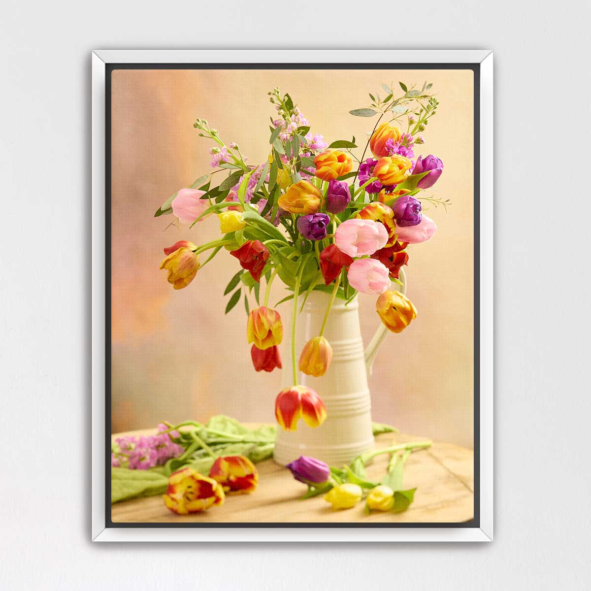 A white vase filled with a vibrant bouquet of tulips in various colors, including pink, yellow, orange, and purple, sits on a wooden surface.