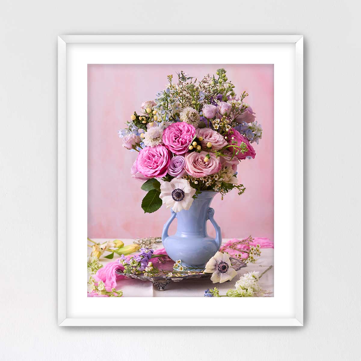 A framed image of a vase filled with a variety of colorful flowers, including pink roses, white lilies, and purple and white flowers, set against a pink background.