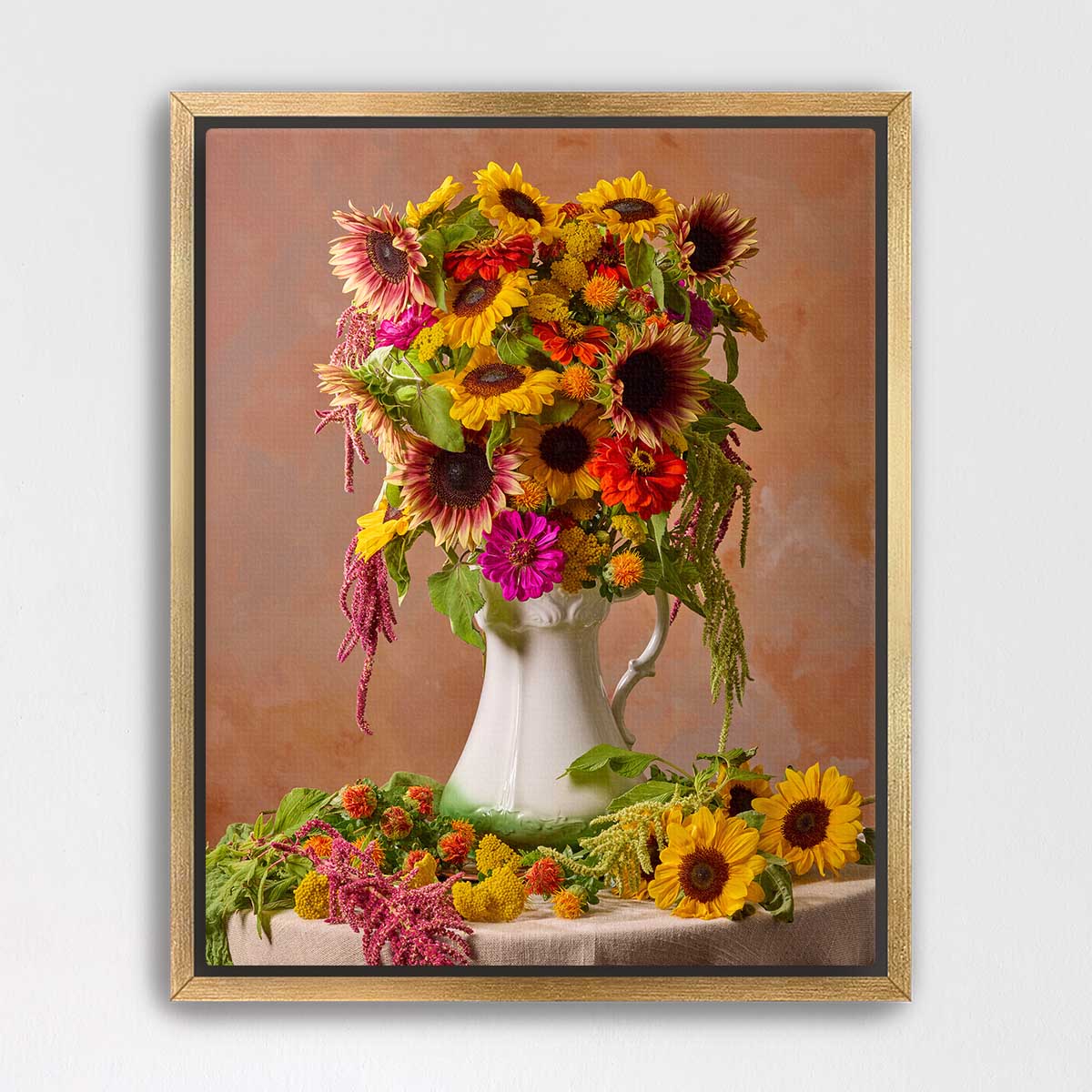 A white vase filled with a vibrant bouquet of sunflowers and other colorful flowers sits on a table, surrounded by additional flowers.