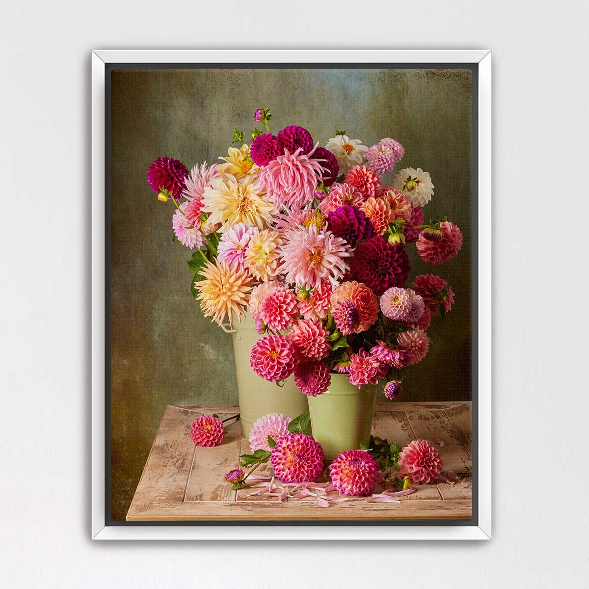A framed still life photograph depicting a bouquet of vibrant pink and white dahlias arranged in two green vases on a wooden surface.