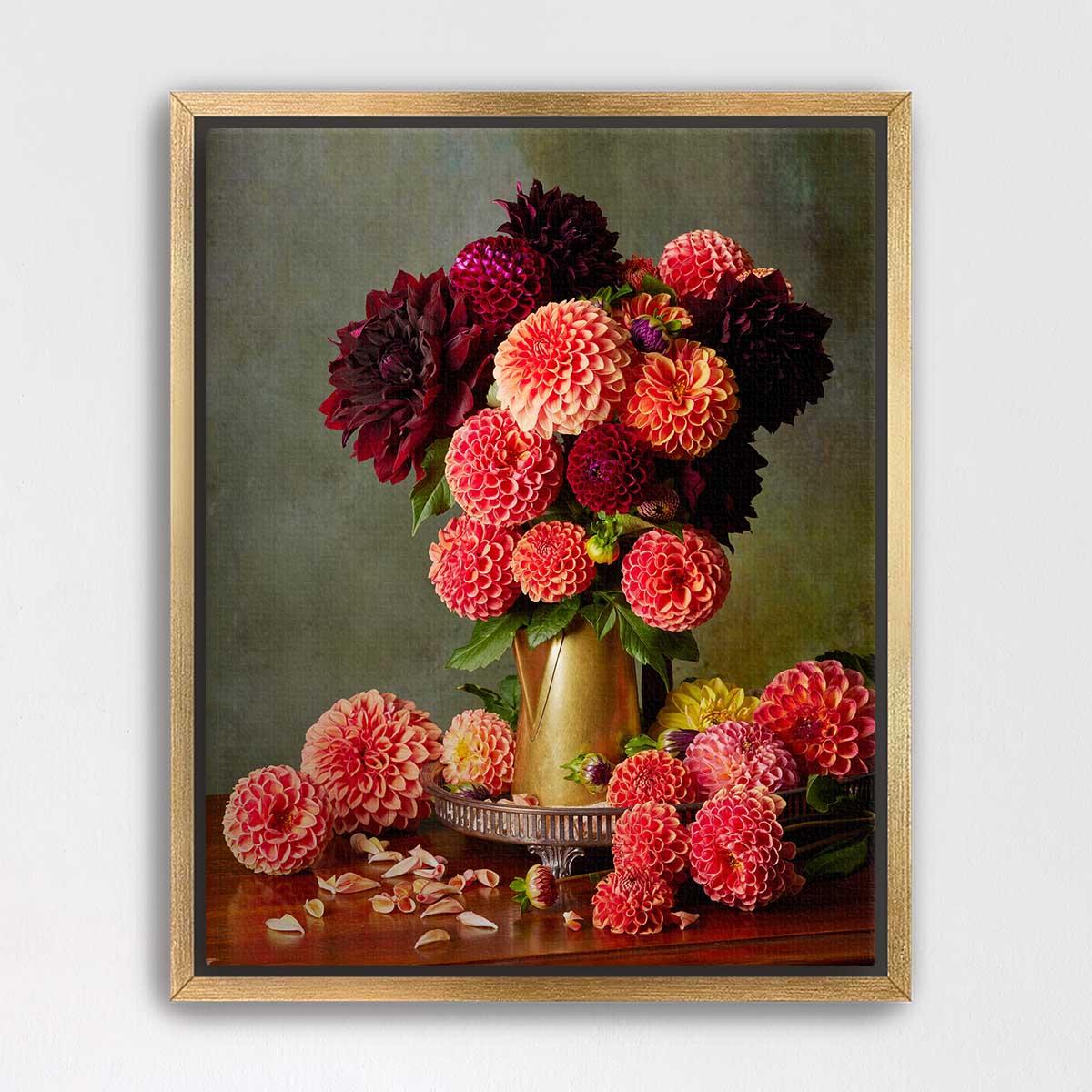 A framed still life painting depicting a vase filled with a variety of colorful dahlias, including red, pink, and yellow flowers, along with some fallen petals on a wooden surface.