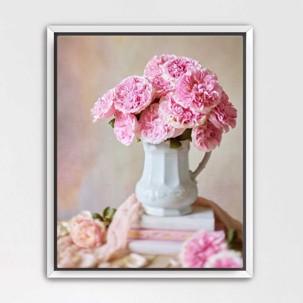 A white vase filled with pink carnations sits on top of a stack of books, creating a charming and elegant still life composition.