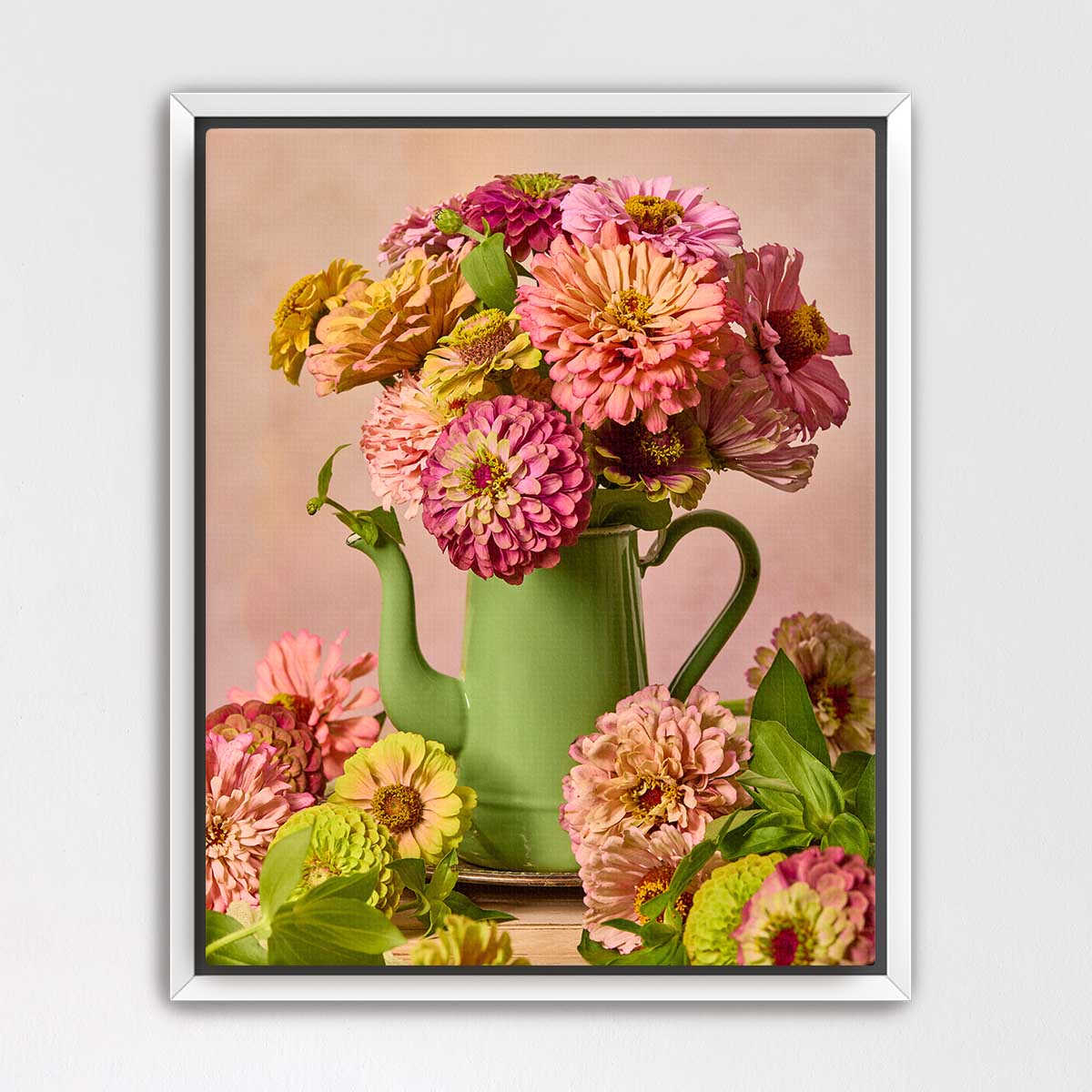A green teapot filled with a vibrant bouquet of pink, yellow, and white flowers sits on a wooden surface, surrounded by additional flowers.