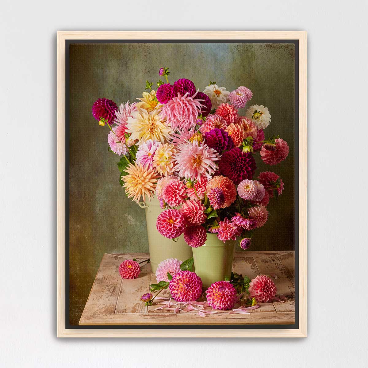 A framed image of a bouquet of colorful dahlias in two green vases, placed on a wooden table against a green background.
