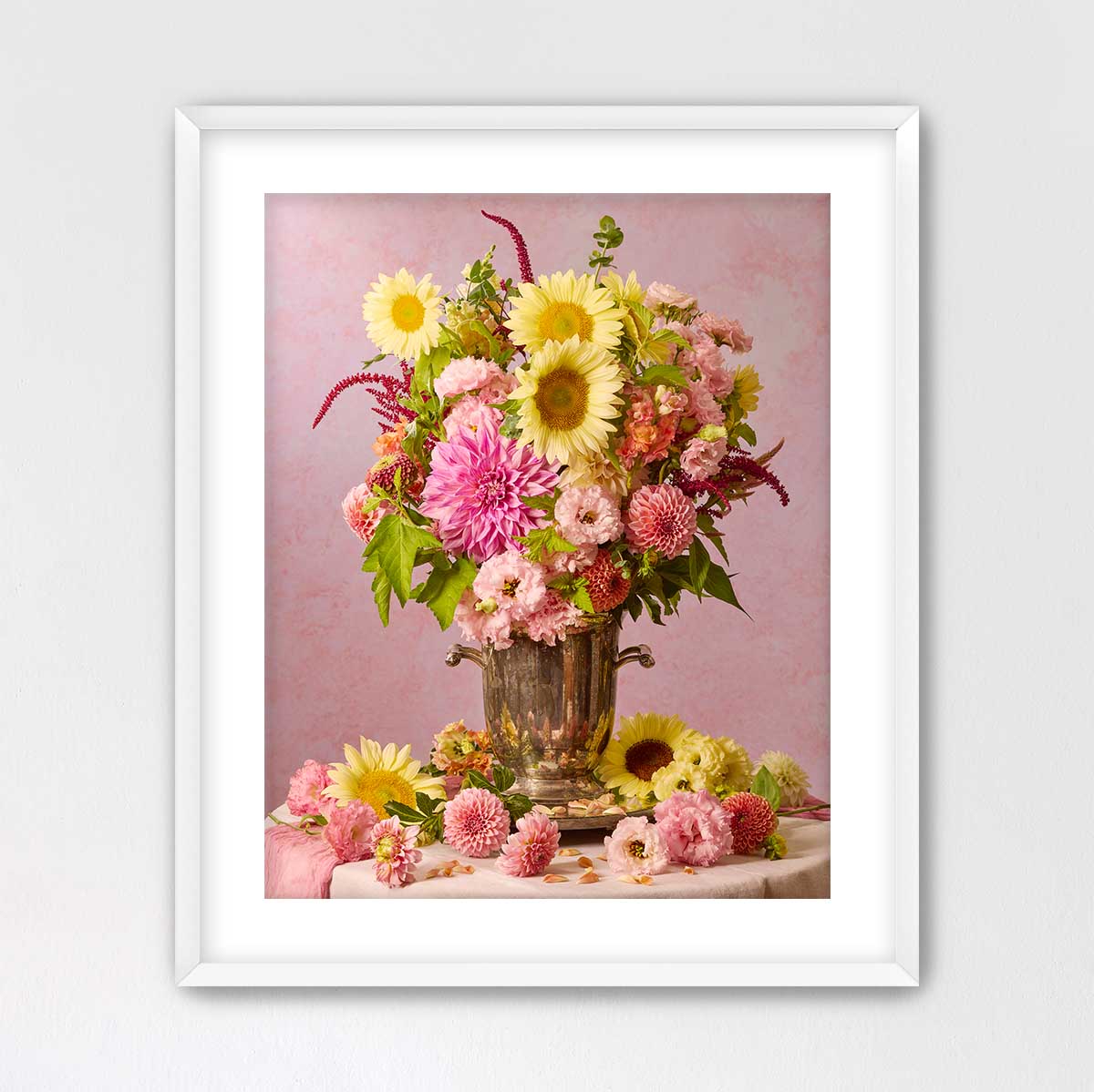 A framed photograph of a bouquet of colorful flowers, including sunflowers, dahlias, and other blooms, arranged in a vase on a table.
