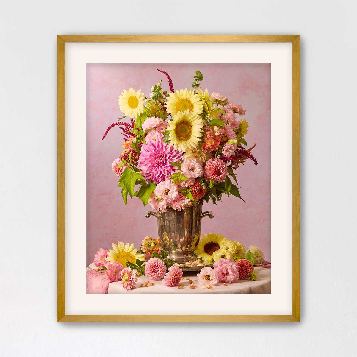 A framed photograph of a vase filled with a variety of colorful flowers, including sunflowers, dahlias, and other blooms, set against a pink background.