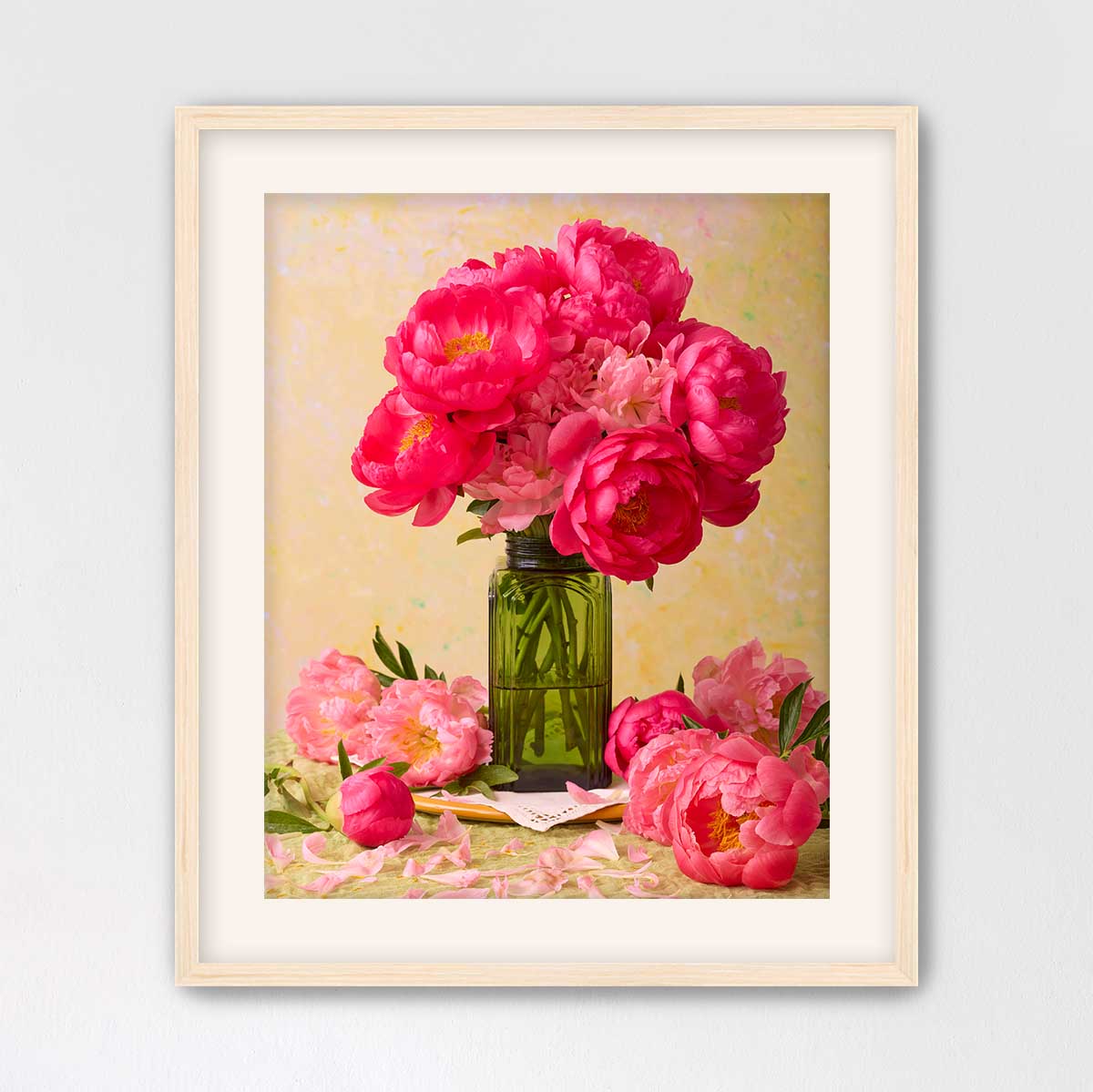 A framed image of a bouquet of pink peonies in a green vase, with additional pink peonies and a green vase on a table.