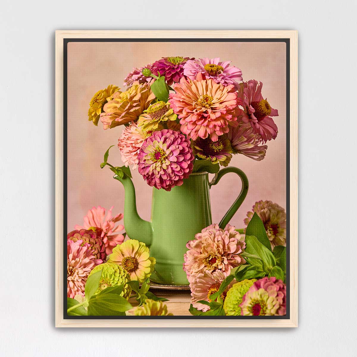 A green vase filled with a vibrant bouquet of pink, yellow, and orange flowers sits on a wooden surface against a pink background.